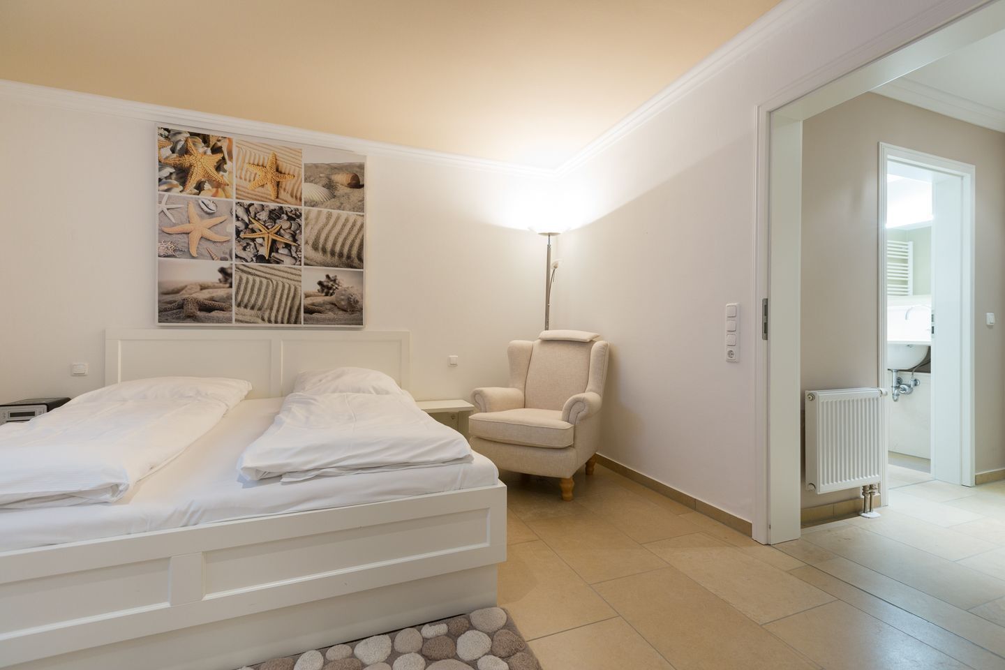 Ein Schlafzimmer mit einem Bett, einem Sessel, einer Wandleuchte und einem durchgegangenen Tür erkennbaren Badezimmer.