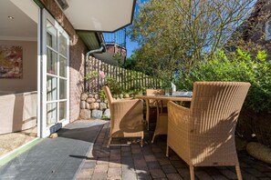 An outdoor patio with wicker furniture, a stone wall, and a clear view of the street. - Carlotta - Long Island Style. Ganz Groß (Wenningstedt-Braderup (Sylt))