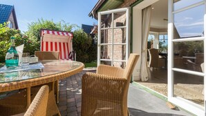 Eine Terrasse mit Korbmöbeln, einem Glastisch und einem rot-weiß gestreiften Stuhl.