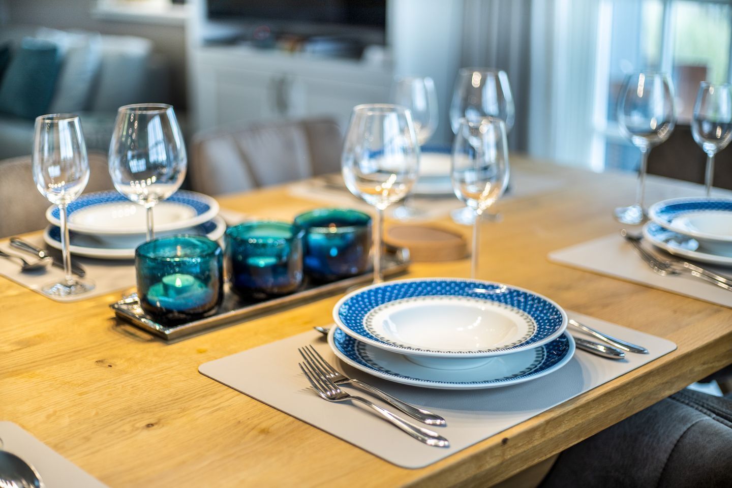 A dining table set with blue and white plates, clear wine glasses, and teal candle holders.