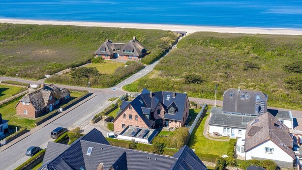 Ett bostadsområde vid kusten med hus, en väg och en strand i bakgrunden.