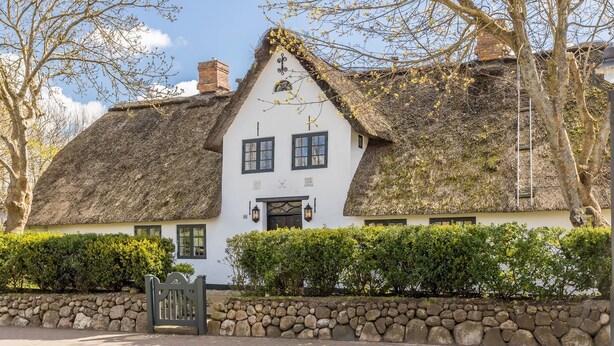 A traditional white building with a thatched roof, a stone wall in front, and a wooden gate.