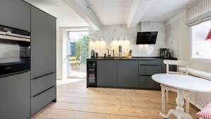 A modern kitchen with grey cabinetry, a built-in oven, and a dining area with a white table and chairs.