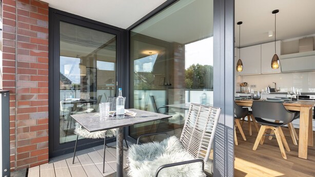 A modern kitchen with wooden cabinets, a dining table with chairs, and a glass door leading to an outdoor area with a table and chairs.