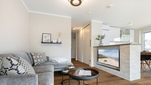 A modern living room with a grey sofa, a coffee table, and a fireplace with a beach view.