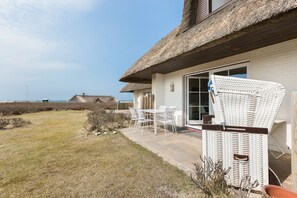 A beach house with a thatched roof, a patio with white wicker furniture, and a view of the sea. - Heimathaten, Haus Blankenese, App. 2 - Ferien Unter Reet im Modernem Ambiente (Wenningstedt-Braderup (Sylt))