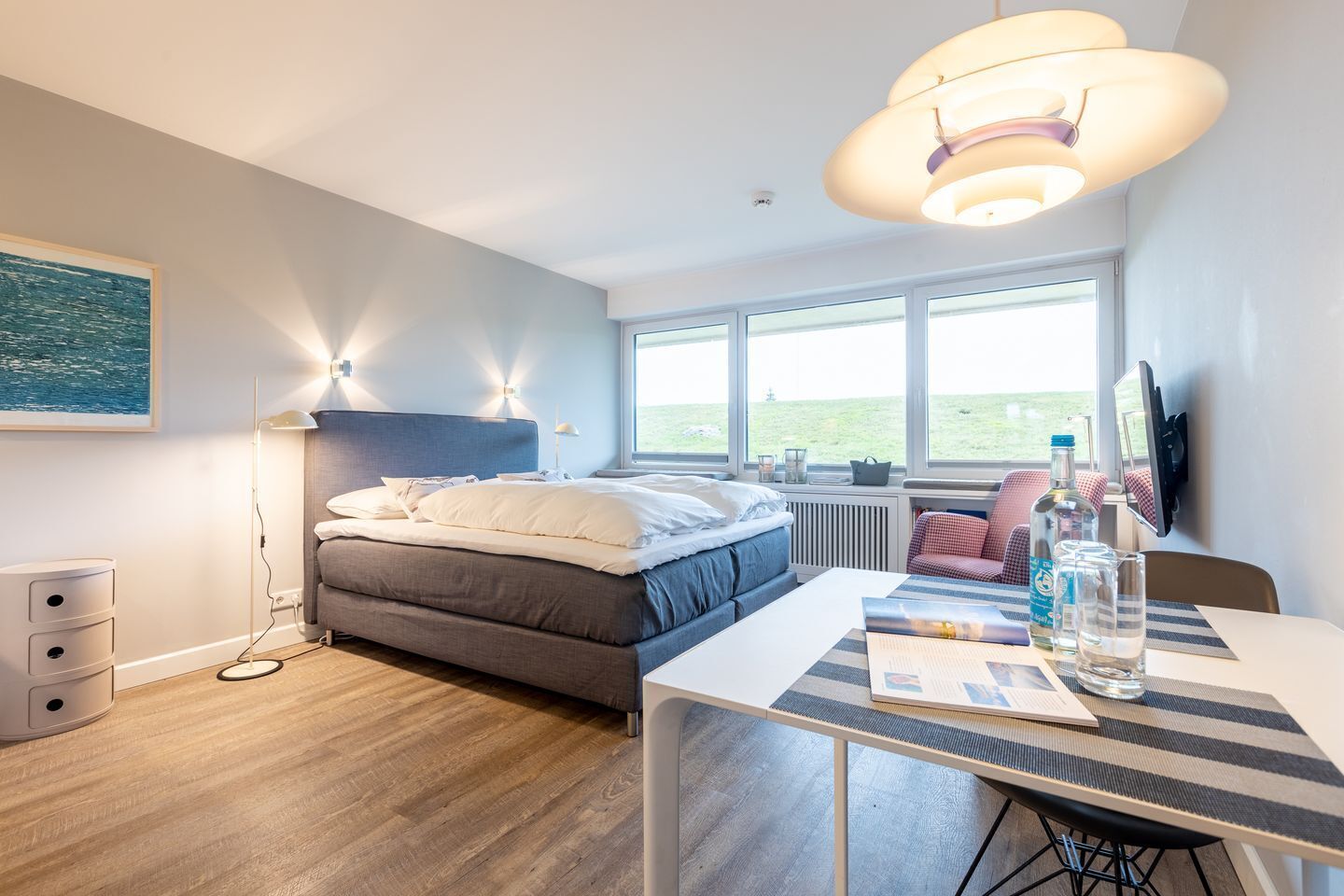 A modern bedroom with a bed, bedside table, and a large window.