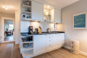 Una cocina moderna con armarios blancos, encimera negra y varios electrodomésticos. Se ve un área de comedor a través de una puerta abierta.
