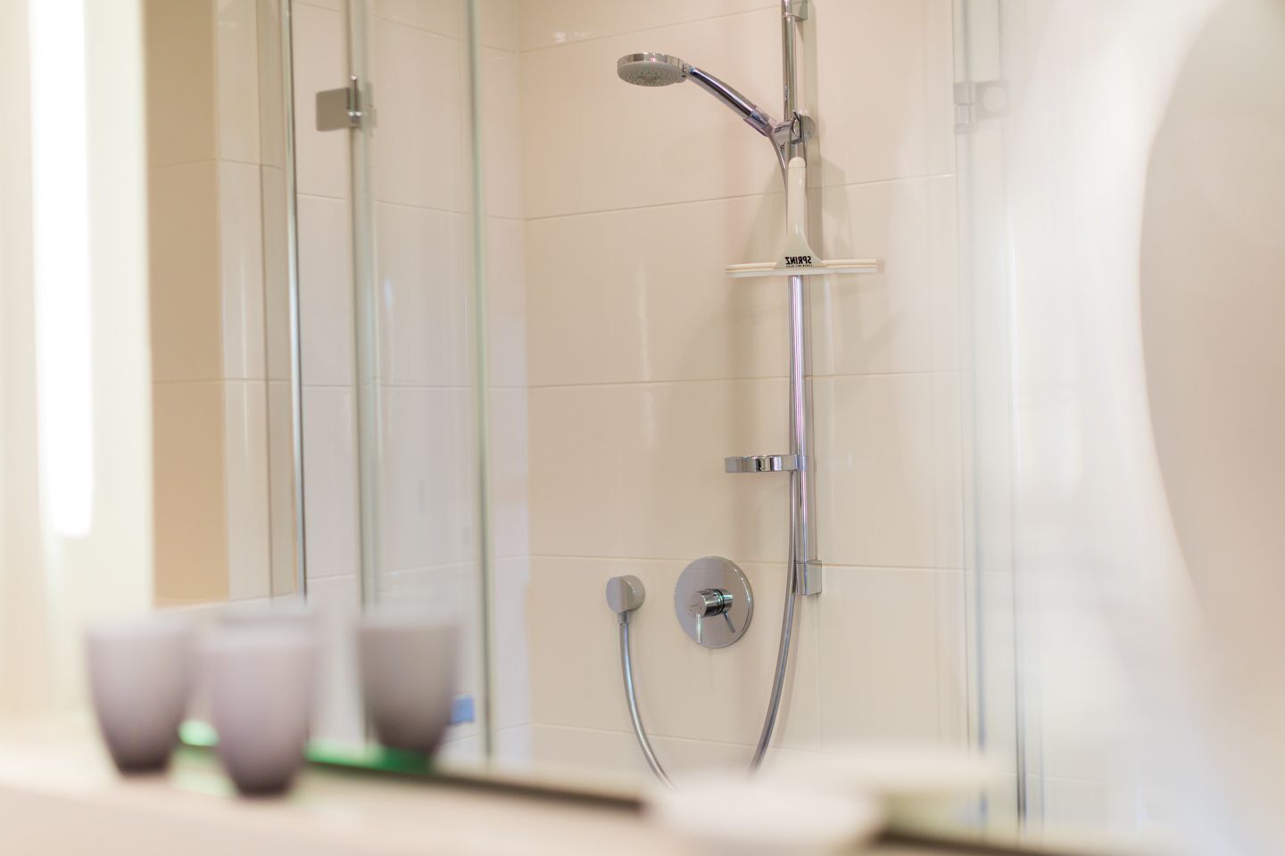 Een moderne badkamer met een douchecabine van glas, een handdouche en een wandmengkraan.