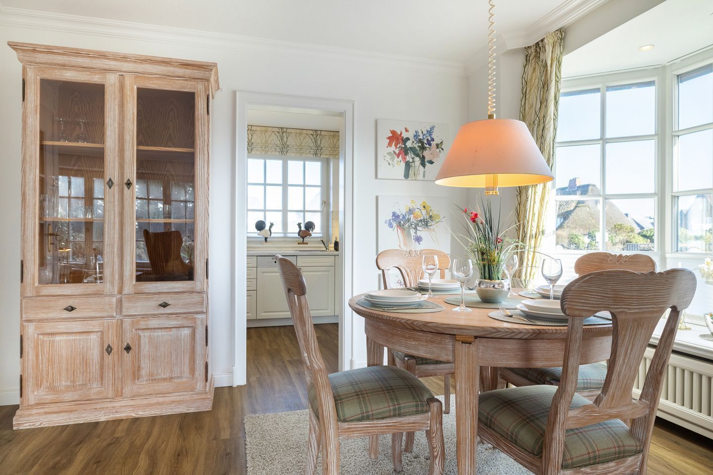 A dining area with a wooden cabinet, a round table with chairs, and a hanging lamp.