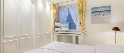 A bedroom with a bed, a window with curtains, a radiator, a painting, and a lamp.