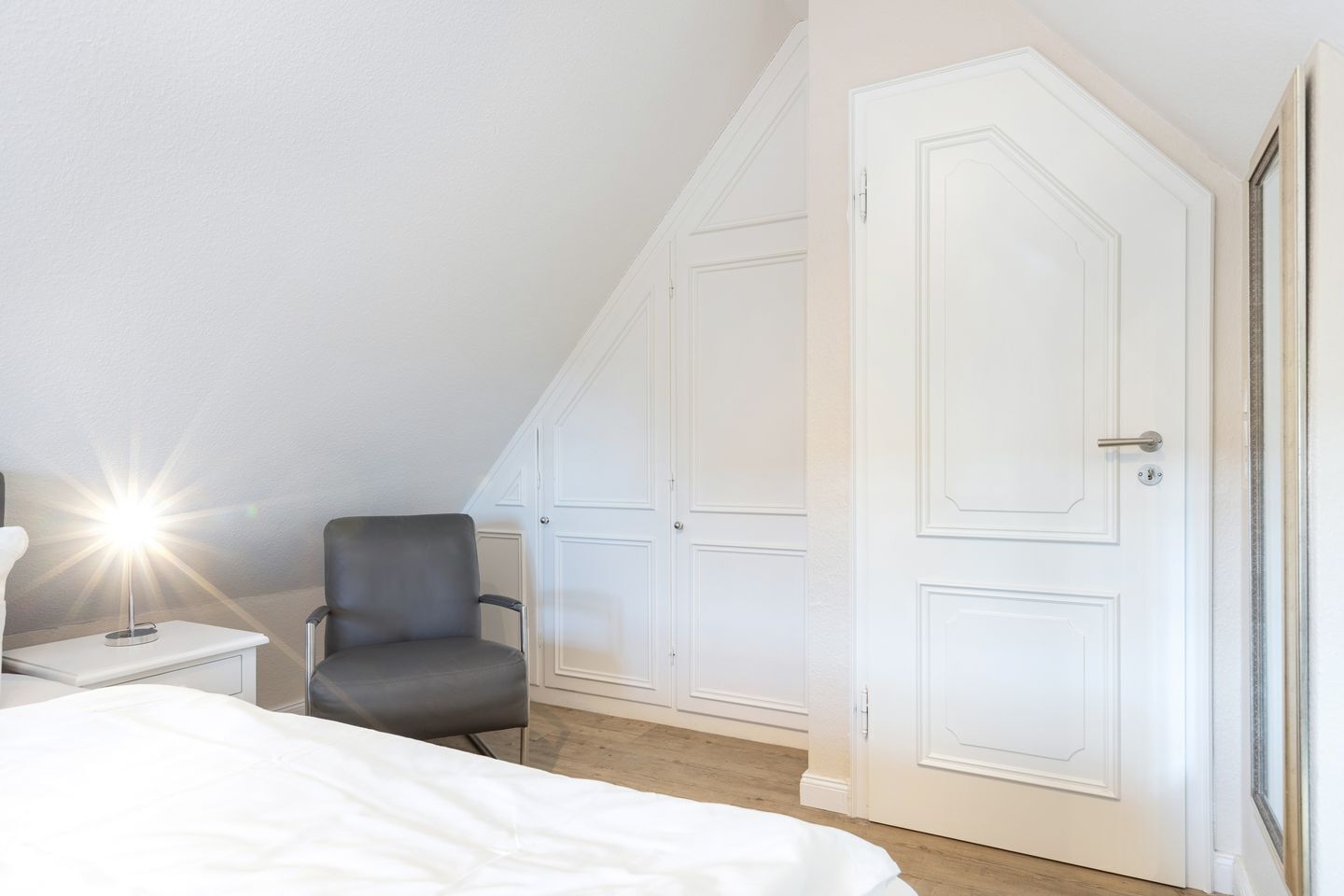 Une chambre à coucher avec un lit, une chaise, une table de chevet et une porte blanche.