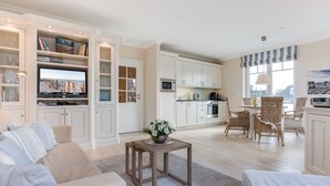 A spacious living room with a large flat-screen TV, a comfortable sofa, and a dining area with wicker chairs. - Landhaus Berthin-bleeg, App. 5 Strandleben - Top Lage. Beach-style Ausstattung. Viel Platz. Alles (Wenningstedt-Braderup (Sylt))