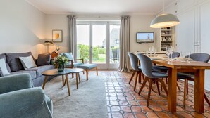 Een ruime woonkamer met een bank, een salontafel en een eethoek met stoelen en een tafel gedekt voor vier personen.