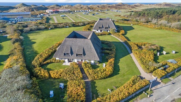 Een luchtbeeld van een landgoed met twee hoofdgebouwen, een groot gazon en een glooiend landschap op de achtergrond.