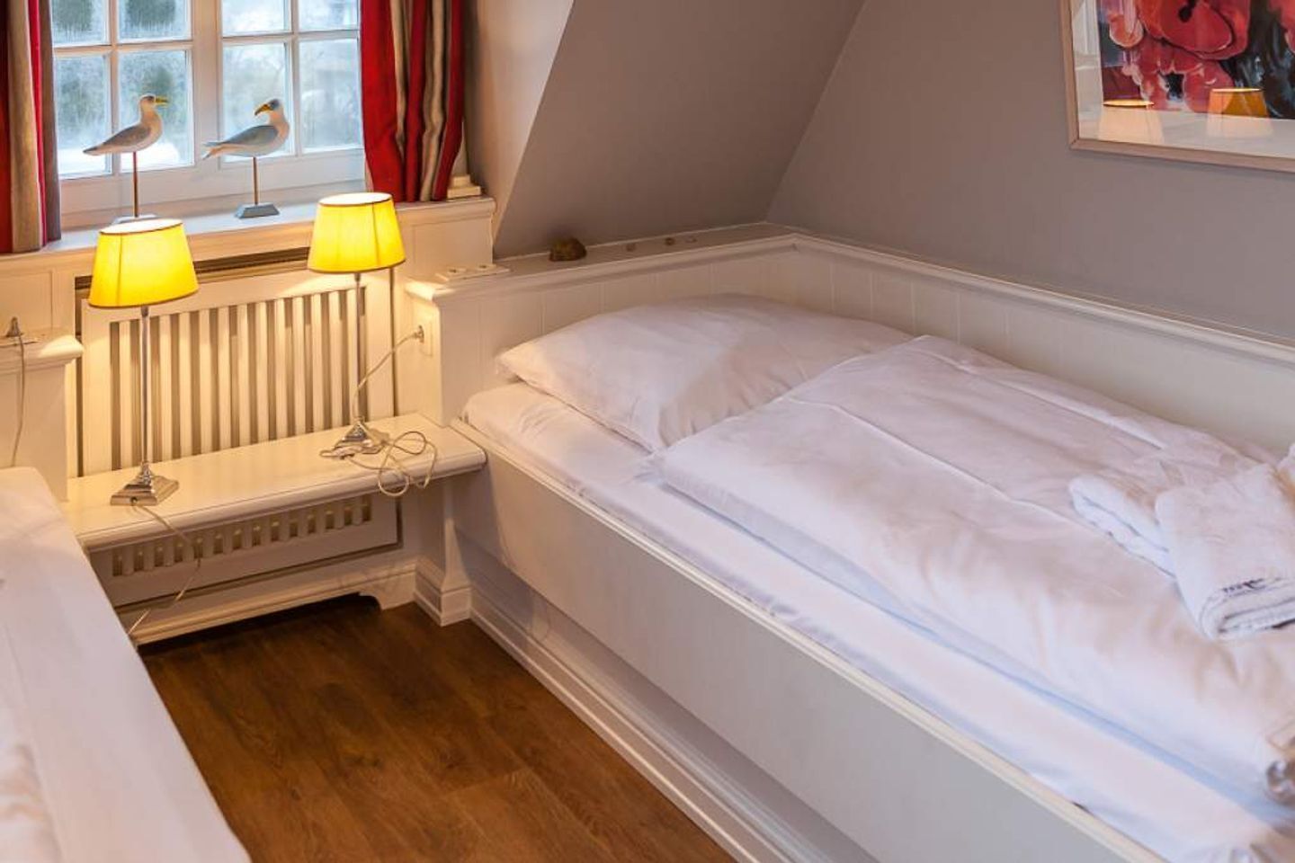 Una cama individual con ropa de cama blanca en una habitación con suelo de madera.