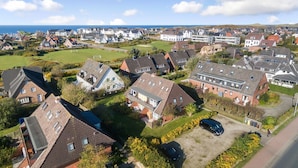 A residential area with houses, a road, and a body of water in the background. - Simokat, Eg-rechts - Sylter Süden. Verbringen Sie Schöne Ferien in Wenningstedt (Wenningstedt-Braderup (Sylt))