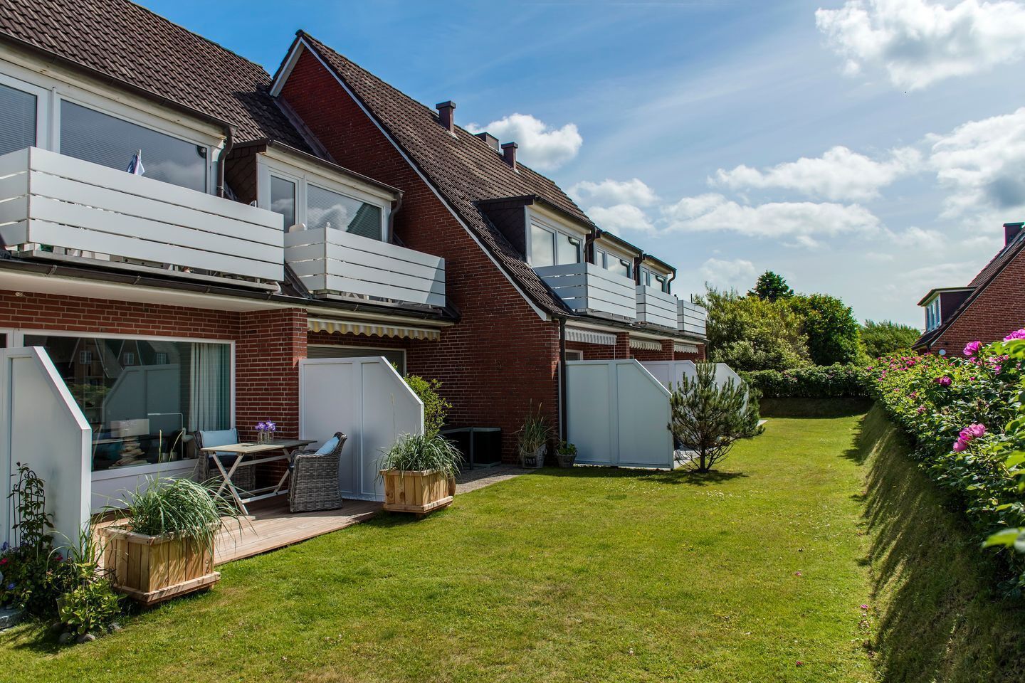 Een huis met twee verdiepingen, een balkon, een overdekt terras en een verzorgd gazon.