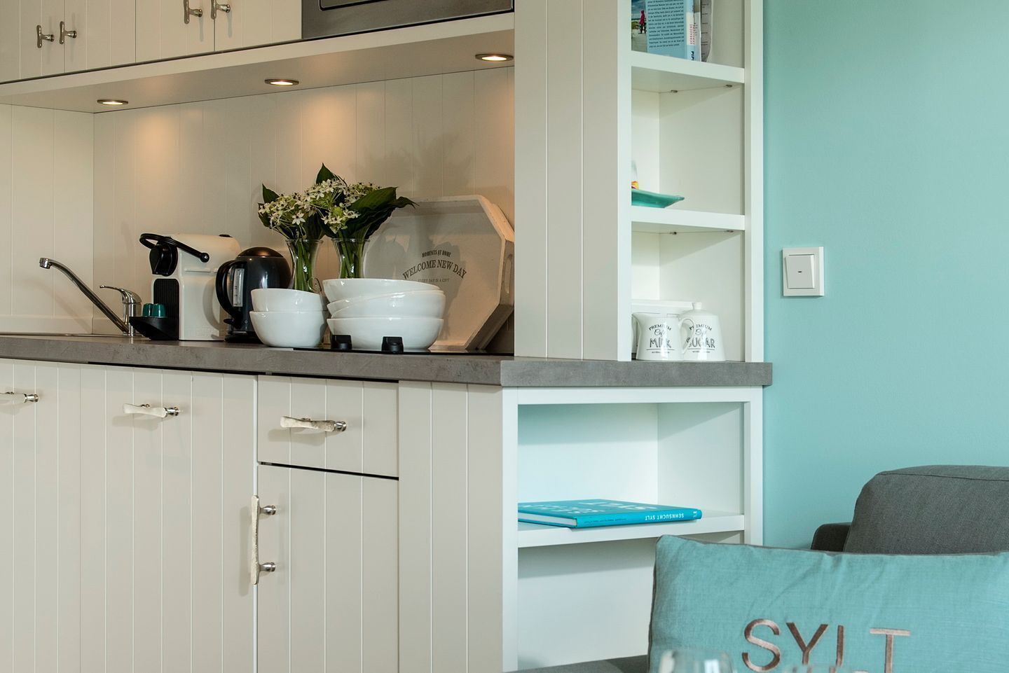 A kitchen with white cabinets, a countertop with bowls and a coffee maker, and a teal wall.