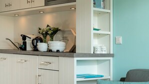 A kitchen with white cabinets, a countertop with bowls and a coffee maker, and a teal wall.