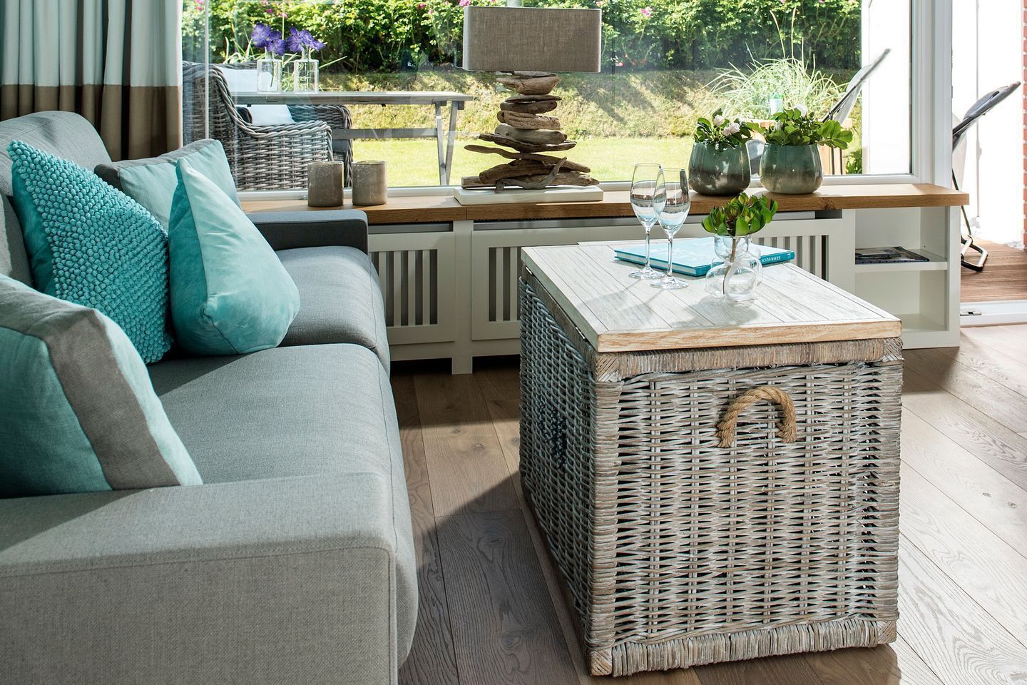 Ein modernes Wohnzimmer mit einem grauen Sofa, einem Korpus-Couchtisch und Blick auf den Garten durch große Fenster.