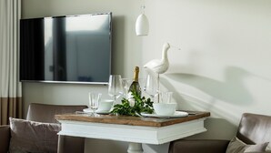 A dining table with a white pedestal base, surrounded by brown leather chairs. A flat-screen TV is mounted on the wall above the table.
