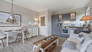 A modern kitchen with grey cabinets, a wooden dining table, and a cozy living area with a sofa and a coffee table. - Inselliebe, App. 18 - Inselliebe Pur! Viel Mehr Sylt-style Können Sie Nicht Buchen (Wenningstedt-Braderup (Sylt))