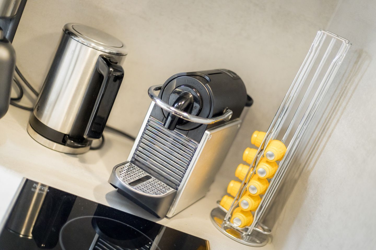 A kitchen area with a coffee machine, a kettle, and a container holding yellow bottles.