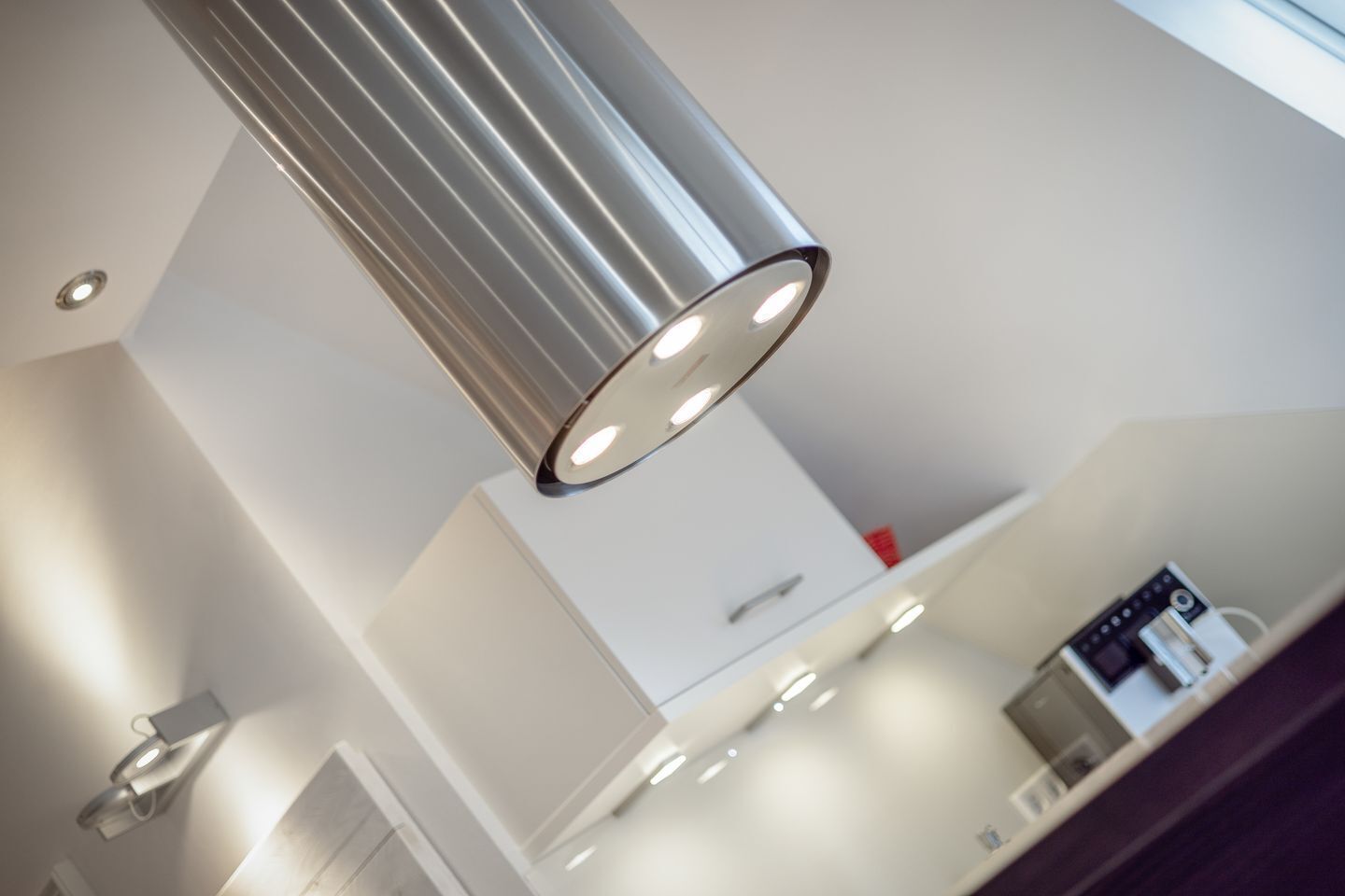 Een moderne keuken met een roestvrijstalen hanglamp, witte keukenkastjes en een ingebouwde koffiemachine.