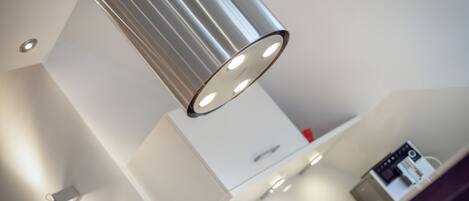 Een moderne keuken met een roestvrijstalen hanglamp, witte keukenkastjes en een ingebouwde koffiemachine.