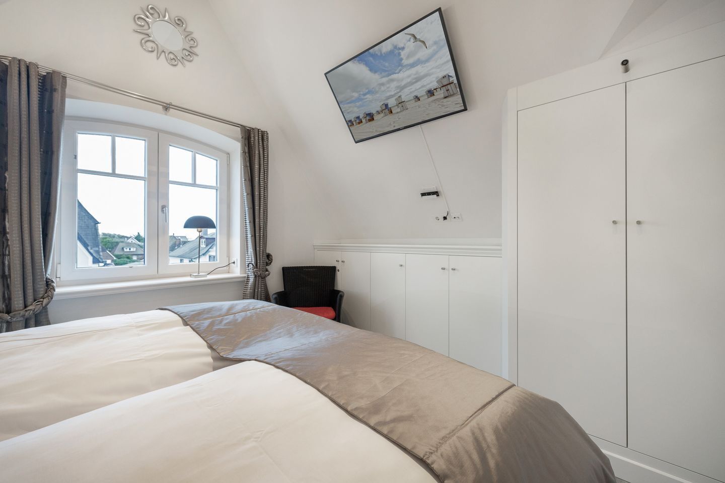 A bedroom with a bed, a chair, a wardrobe, a window with curtains, and a wall-mounted picture.