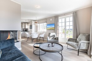 A modern living room with a fireplace, a dining area, and a kitchen in the background. - Lille Wung - Ruhige und Dennoch Zentrale Lage? (Wenningstedt-Braderup (Sylt))