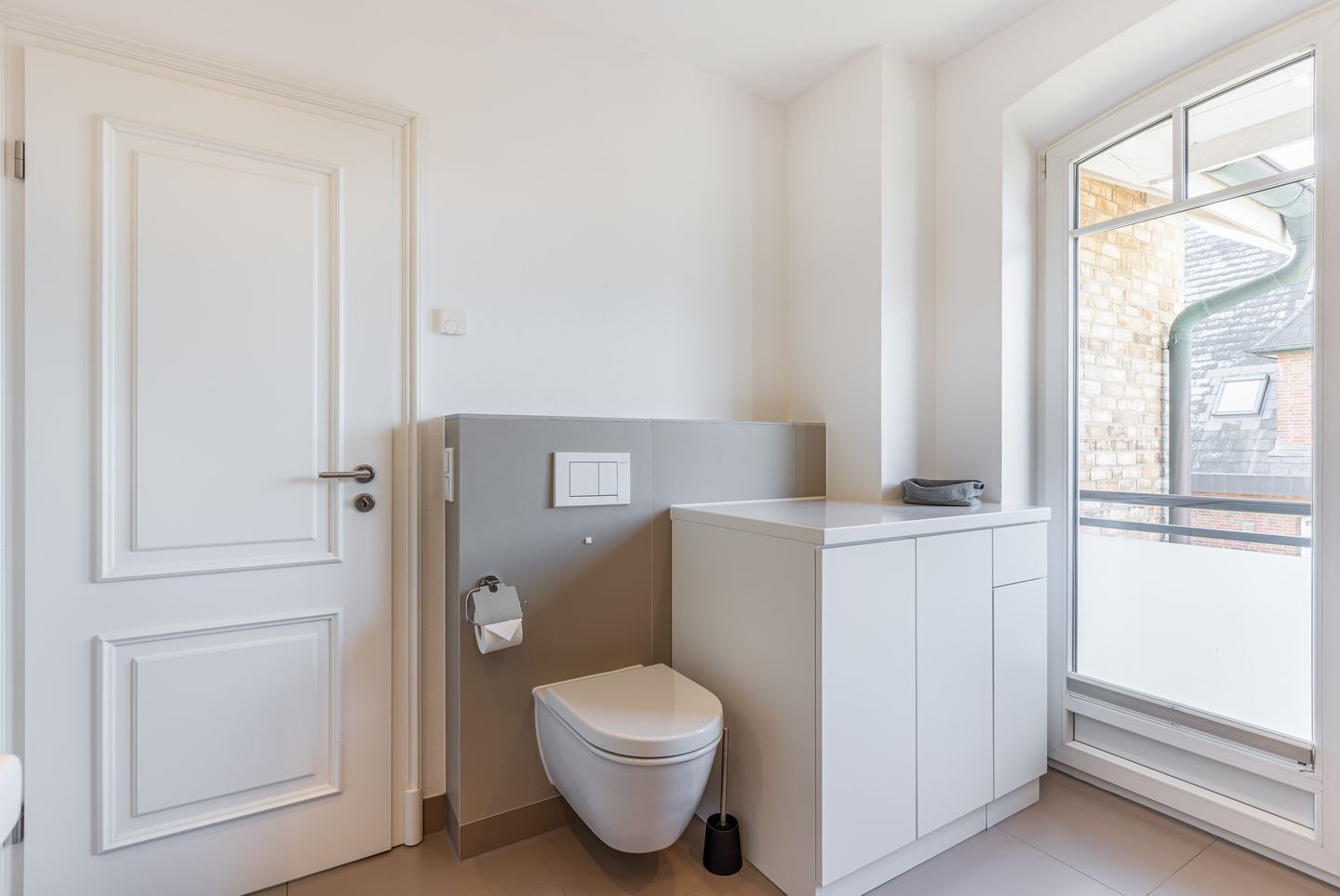 A bathroom with a toilet, a towel dispenser, and a window with a view of buildings.