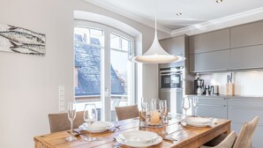 Una cocina moderna con armarios grises, una mesa de comedor de madera dispuesta con platos, vasos y cubiertos, y una lámpara colgante arriba.