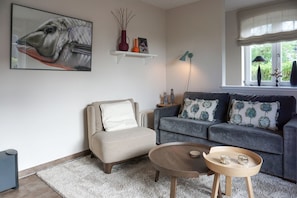 A living room with a sofa, armchair, coffee table, and a painting on the wall.