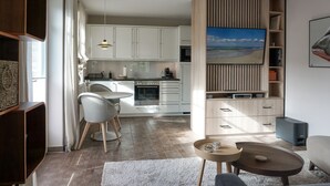 Eine moderne Küche mit weißen Schränken, einem Essbereich mit rundem Tisch und Stühlen, einem integrierten Fernseher und einer gemütlichen Sitzecke mit Couch und Couchtisch.
