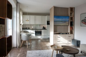 A modern kitchen with white cabinets, a dining area with a round table and chairs, a built-in TV, and a cozy seating area with a coffee table and sofa. - Landhaus Berthin-bleeg, App. 4 Buhne 4 - Top Lage. Luxuriöse Ausstattung. Wellness im Hause (Wenningstedt-Braderup (Sylt))