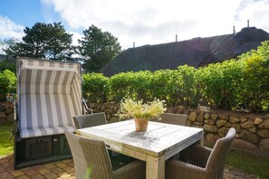 A patio with a striped outdoor sofa, a table with chairs, and a potted plant. - Landhaus Berthin-bleeg, App. 4 Buhne 4 - Top Lage. Luxuriöse Ausstattung. Wellness im Hause (Wenningstedt-Braderup (Sylt))