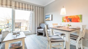 Un comedor con una mesa dispuesta para dos personas, un sofá y un televisor en la pared.