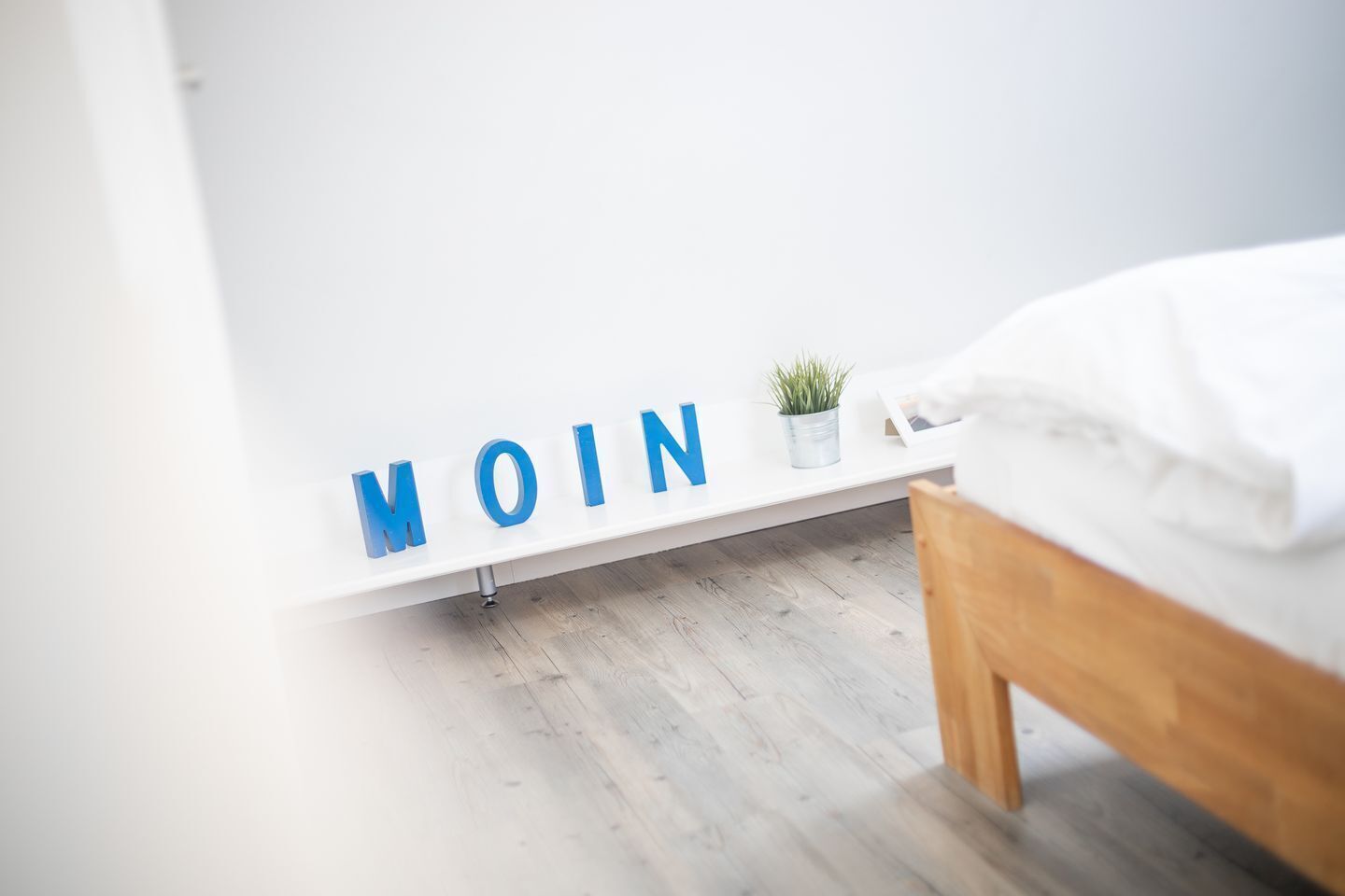 A bedroom with a bed, a white wall, and a shelf with the word "MOIN" in blue letters.