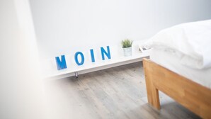 Un dormitorio con cama, pared blanca y estante con la palabra 'MOIN' en letras azules.