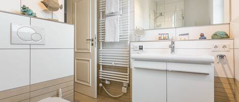 Un baño moderno con inodoro, lavamanos con espejo, toallero y zona de ducha.