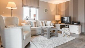 A modern living room with a sofa, armchair, coffee table, and a TV on a wooden cabinet. - Landhaus Berthin-bleeg, App. 7 Lichtblick OG Rechts - Zwei Raum Appartement im 1. OG auf Einer Ebene (Wenningstedt-Braderup (Sylt))