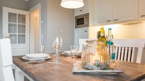 A dining area with a wooden table set for two, a wine glass, a glass pitcher, and a bottle of wine. - Landhaus Berthin-bleeg, App. 7 Lichtblick OG Rechts - Zwei Raum Appartement im 1. OG auf Einer Ebene (Wenningstedt-Braderup (Sylt))