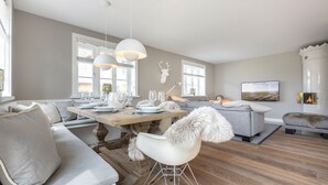 Ein modernes Wohnzimmer mit Essbereich, grauen Sofas, einem Kamin und einem großen Fernseher.