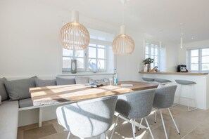 Una cocina moderna con una mesa de comedor de madera, sillas tapizadas en gris y luces colgantes.