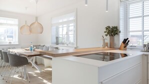 Cozinha moderna com ilha central, armários brancos, iluminação pendente e uma grande janela que proporciona luz natural.