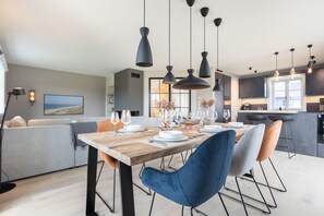 Un'area pranzo moderna con tavolo in legno, sedie blu e arancioni e lampade a sospensione.