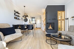 Una sala de estar moderna con chimenea, un comedor con sillas y una cocina al fondo.