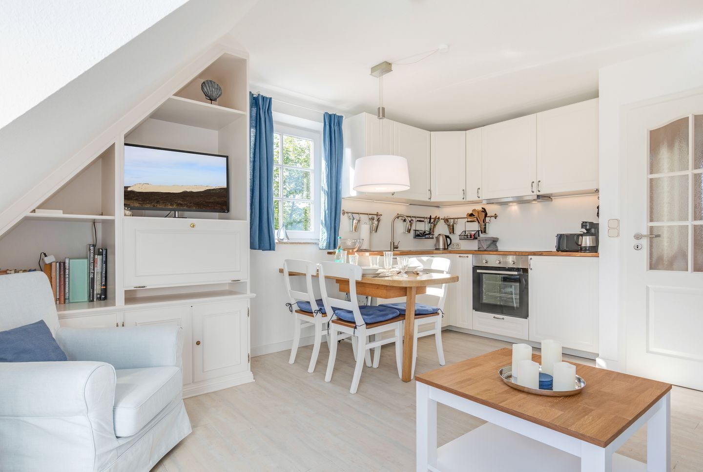 Una cocina moderna con armarios blancos, una mesa de comedor con sillas y un televisor montado en la pared.